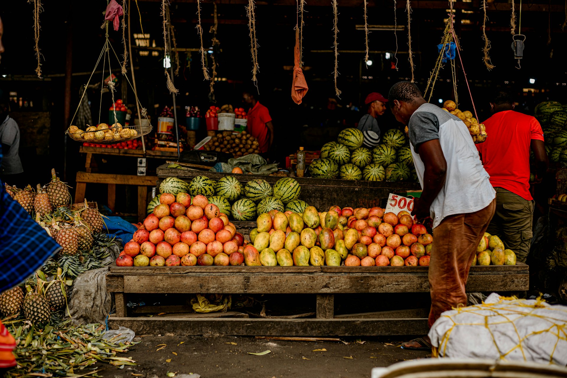 A vendor standing in front of a fruit stand at an open-air market